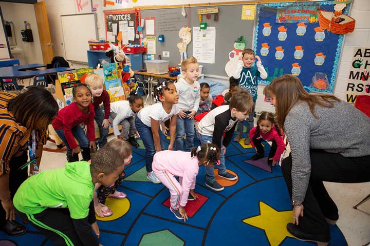 A group of preschoolers doing whole group exercises with their teacher.