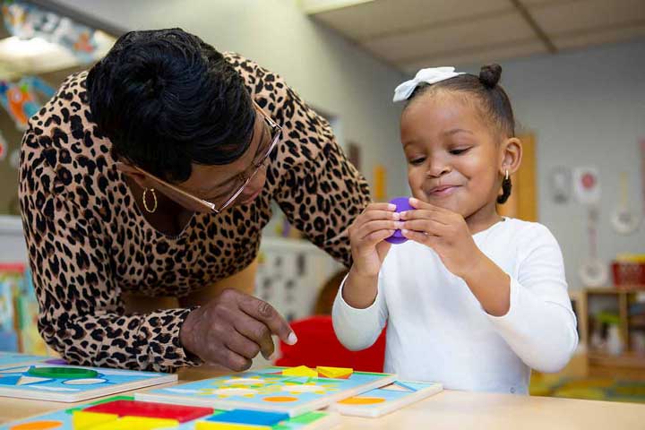 A teacher looking on as a girl feels good about putting together a puzzle.