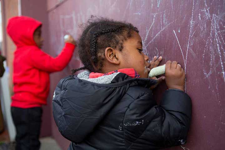 A child writing on a chalkboard outside.