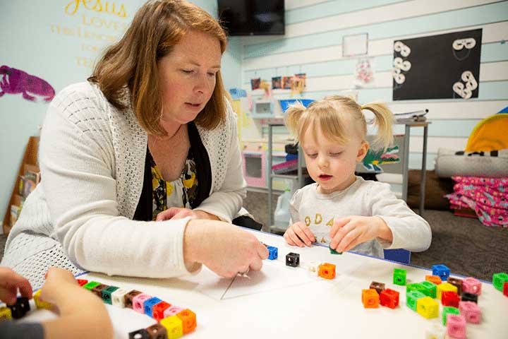 Preschool teacher helping a young child build a triangle with blocks.